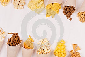 Summer fun fast food - different crunchy snacks in craft paper cornet as decoration border on soft white wood board.