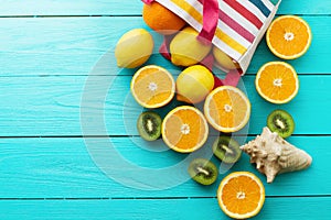 Summer fun time and fruits on blue wooden background. Orange, lemon, kiwi fruit in bag and shell