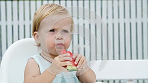 Summer, in the garden, funny one-year-old blond girl eating watermelon