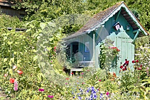 Wooden turquoise summerhouse in beautiful summer garden with lots of blooming flowers photo