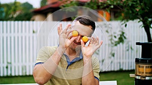 summer, in the garden. a man, father, having fun with his family outdoors, twisting, applying mandarins to his eyes