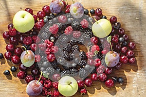 Summer gifts, wet and ripe blackberries, red cherries, raspberries, black currants, apples and plums lie on a wooden surface