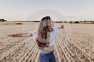 Summer Girl enjoying nature on yellow field. Beautiful young woman dancing Outdoors. Long hair in the wind. Happiness and