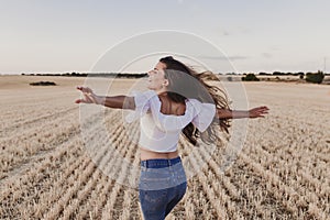 Summer Girl enjoying nature on yellow field. Beautiful young woman dancing Outdoors. Long hair in the wind. Happiness and