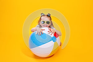 Summer girl wearing sunglasses with ball laughing on yellow background