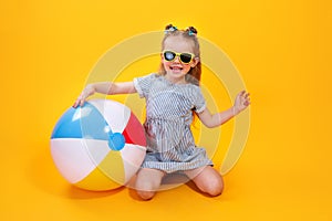 Summer girl wearing sunglasses holding ball laughing on yellow background