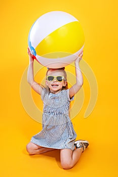 Summer girl wearing sunglasses holding ball laughing on yellow background