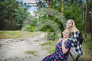 In summer  a grandmother sits on a bench in the forest and her granddaughter hugs her. they are happy