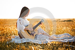 Summer is a great dream time. Beautiful girl playing the guitar in a wheat field