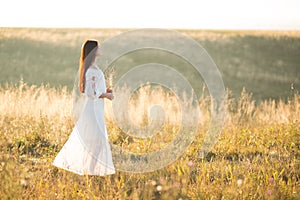 Summer is a great dream time. Beautiful girl in white dress running on the autumn field of wheat at sunset time