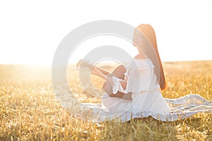 Summer is a great dream time. Country girl sitting with guitar at wheat field