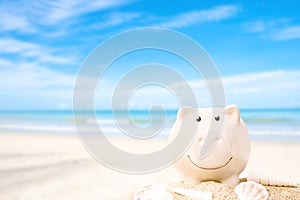 Summer happy piggy bank on sand beach over blurred tropical blue sea background