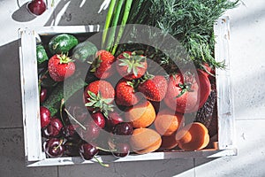 Summer harvest of fruits and vegetables in white wooden box on tile background. Plant-based diet concept