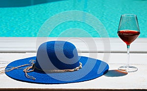 Summer hat and glass of wine in front of the pool.