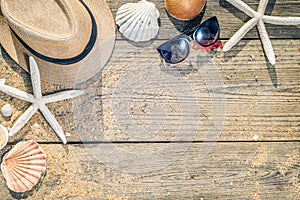 Summer hat, shells and sun glasses on wooden and sandy background