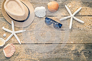 Summer hat, shells and sun glasses on wooden and sandy background