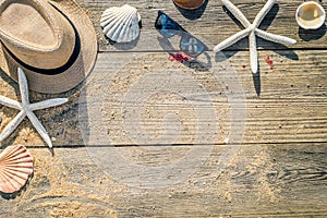 Summer hat, shells and sun glasses on wooden and sandy background