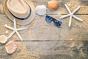 Summer hat, shells and sun glasses on wooden and sandy background