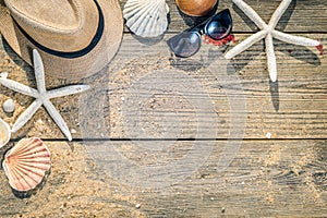 Summer hat, shells and sun glasses on wooden and sandy background