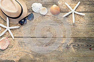 Summer hat, shells and sun glasses on wooden and sandy background