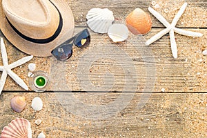 Summer hat, shells and sun glasses on wooden and sandy background