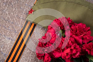 Summer hat of a soldier with a red star and St. George ribbon next to a becket of carnations, May 9 holiday, Victory Day