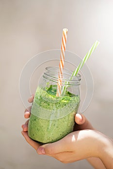 Summer healthy detox drink, blended green smoothie in the bright midday, in the hands of a girl, selective focus