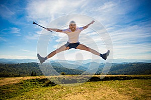 Summer hiking in mountains. Young tourist man in cap with hands up on top of mountains admires nature