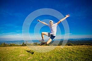 Summer hiking in mountains. Young tourist man in cap with hands up on top of mountains admires nature