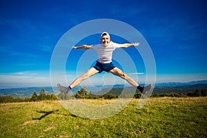 Summer hiking in mountains. Young tourist man in cap with hands up on top of mountains admires nature