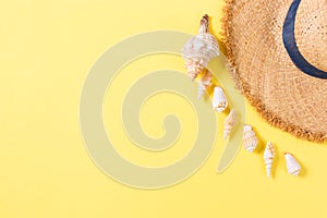 Summer holiday background with straw hat and seashells on yellow background top view with copy space