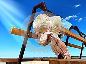 Summer holiday on beach ,women hat with bow beachwear  blue jeans on wooden bench  sky  with white clouds beach with white  sand ,