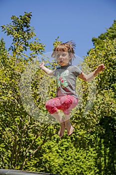 Summer holiday concept. Little cute child girl having fun outdoors and she jumping for joy on a trampoline