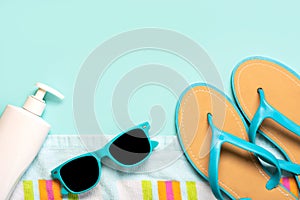 Summer holiday concept.Top view of blue flip flops,beach towel, blue sunglasses and bottle of sunscreen with copy space
