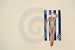 Summer holiday fashion concept - tanning girl wearing sun hat at the beach on a white sand shot from above.Top view from drone.