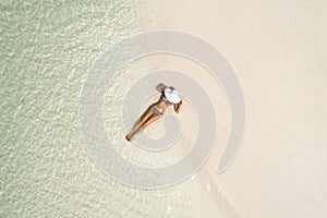 Summer holiday fashion concept - tanning girl wearing sun hat at the beach on a white sand shot from above.Top view from drone.