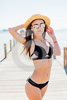 Summer holiday fashion concept - tanning woman wearing sun hat at the sea on a wooden pier