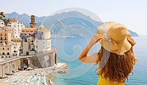 Summer holiday in Italy. Back view of young woman holding her hat with Atrani village on the background, Amalfi Coast, Italy
