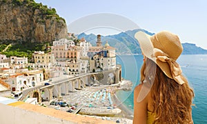 Summer holiday in Italy. Back view of young woman with straw hat and yellow dress with Atrani village on the background, Amalfi