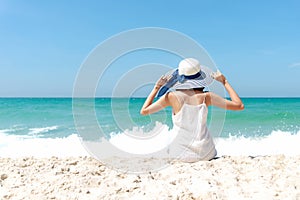 Summer Holiday. Lifestyle woman white dress wearing fashion summer trips sitting on the sandy ocean beach. Happy woman enjoy and r