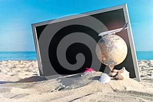 Summer holiday poster. Globe, seashell, airplane and starfish near black desk on sea beach in sunny day. Summer vacation and