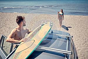 Summer holiday road trip vacation- surfer man at the beach getting ready for extreme surfing.