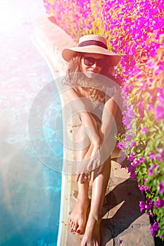 Summer holiday - suntanned sexy woman relaxing near swimming pool, poolside with straw hat and sunglasses