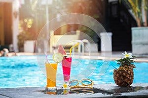 Summer holiday tropical concept. Fresh orange juice and watermelon juice and pineapple on border of a swimming pool