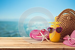 Summer holiday vacation  concept with pineapple juice, beach fashion bag and flip flops on wooden table over sea beach background