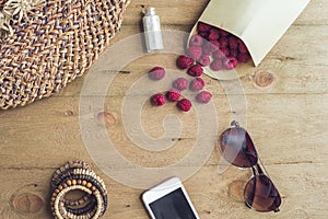 Summer holiday, vacation, relaxation concept. Raspberries, straw hat, smartphone, sunglasses from above, top view, flat lay on woo