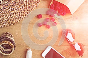 Summer holiday, vacation, relaxation concept. Raspberries, straw hat, smartphone, sunglasses from above, top view, flat lay on woo