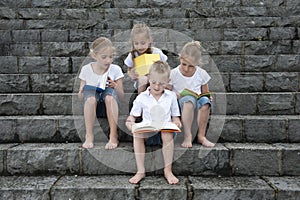 Summer holidays: children with a book seated outdoors on stairs