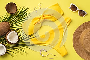 Summer holidays concept. Top view photo of yellow bikini hat stylish sunglasses shell bracelet earrings coconuts and palm leaves