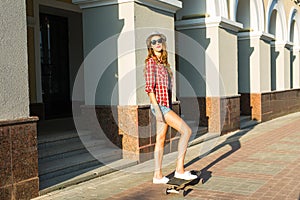 Summer holidays, extreme sport and people concept - happy girl riding modern skateboard on city street